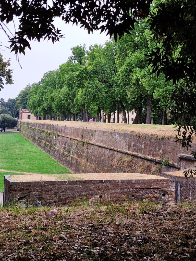  The long red brick defensive walls are surrounded by trees and grass.