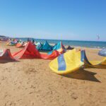 On the sandy beach by the sea lie yellow, red and blue sails for water sports.