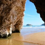 The rocks form the entrance to the cave through which you can see the yellow sand inside and the blue sea outside