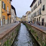 A small stream flows in an old stone canal through the city street between old colorful buildings.
