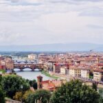 Trees grow on the banks of the river flowing under the bridges, and on one bank stand the buildings of Florence