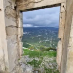 Through the stone window you can see bluish and green hills.