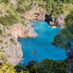 Very blue sea in a small bay surrounded by rocky mountains.
