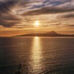 the sun sets over an island by the sea