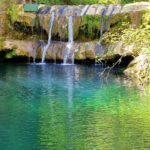 Rivulets of water flow from the concrete wall into a very blue pond.