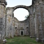Ruins that look like the main nave of a monastery, with walls on the sides, and in front of it is something like a wall with a large open window in the shape of an arch.