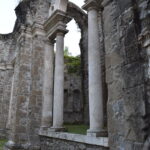 a ruined wall built of stone has two tall columns in the middle forming a window