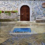 A large sewage pit from which water flows onto the stone street.