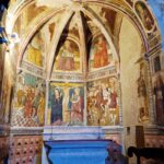 Colorful frescoes depicting saints are painted on the walls, forming a domed ceiling. Below this stands a blue altar, on which stands a cross and two candlesticks.